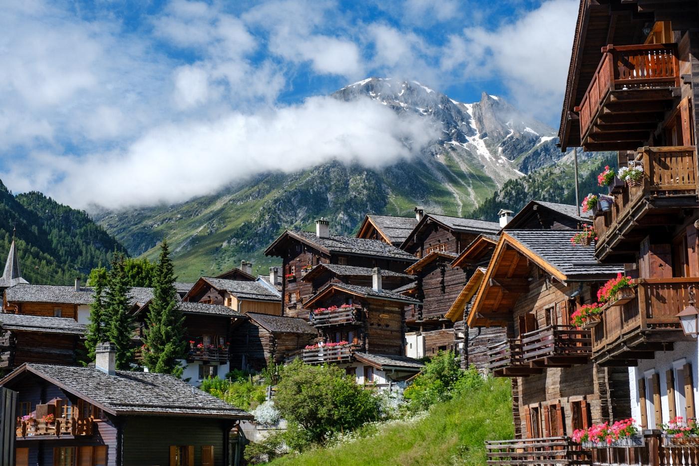 Brown wooden houses near green trees and mountain under white clouds during daytime
