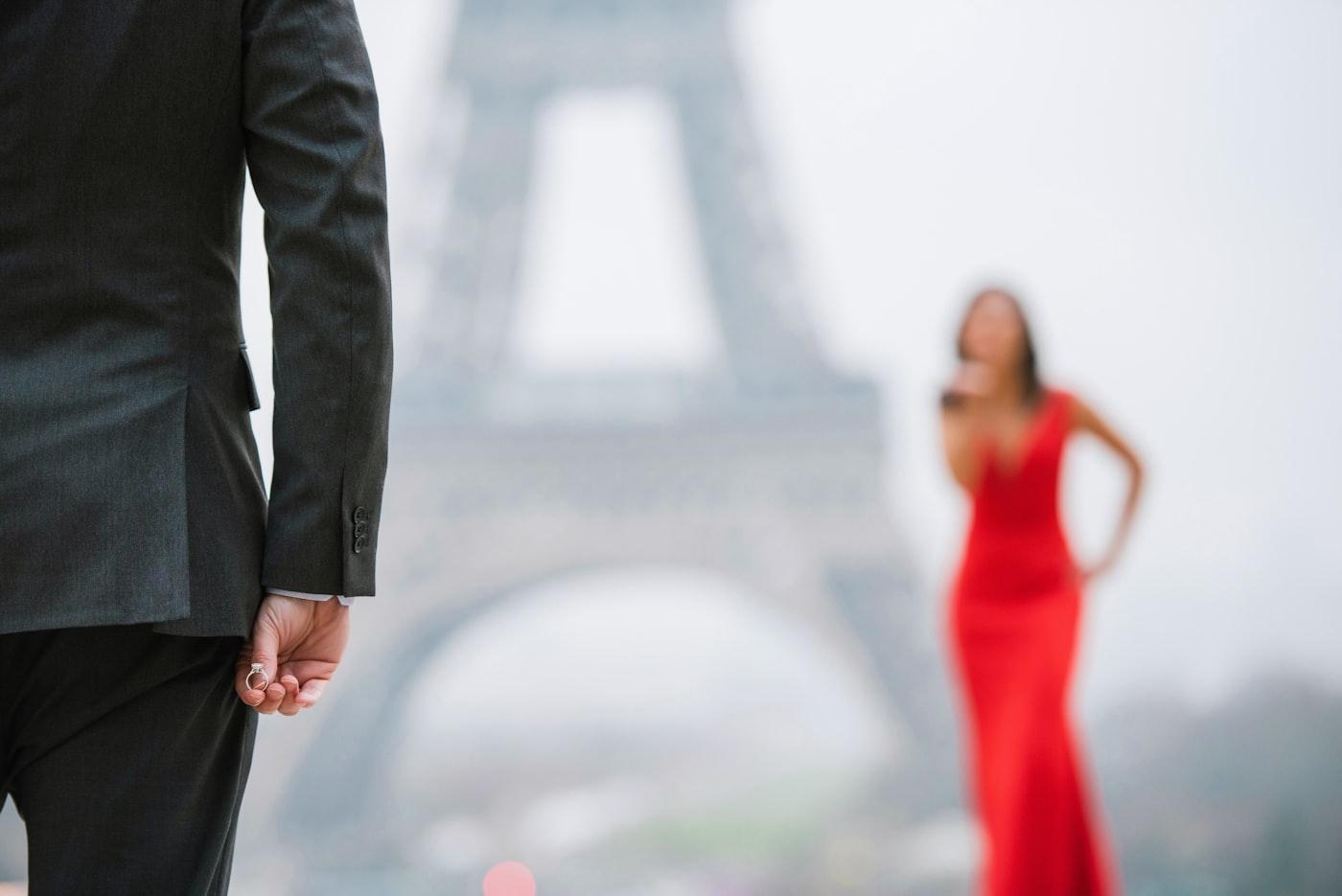 A man holds an engagement ring behind his back at the Trocadéro, the Eiffel Tower in the mist behind
