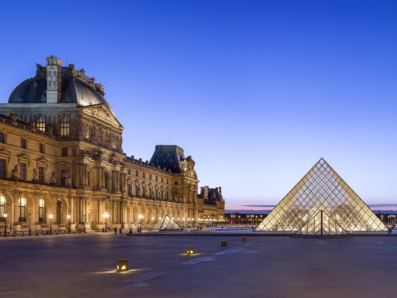 The glass pyramid and the lit facades of the Louvre courtyard at dusk